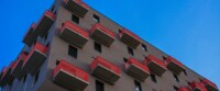 Low-Angle View Of A Vienna Residential Building With Red Balconies Against A Clear Blue Sky.