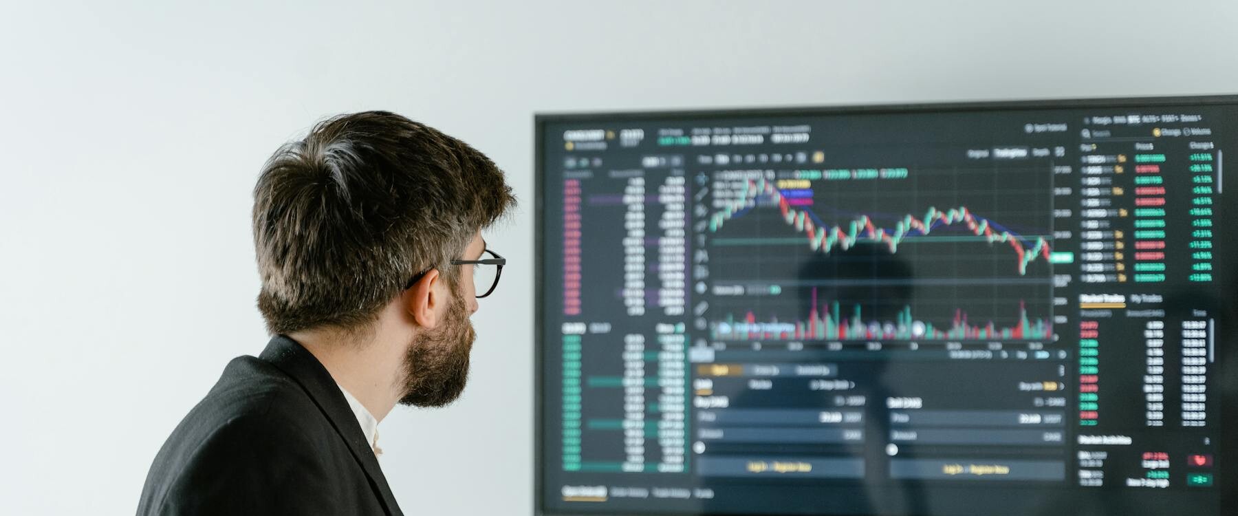 Man Observing Stock Market Data On A Screen And Holding A Tablet, Representing Financial Analysis And Trading.